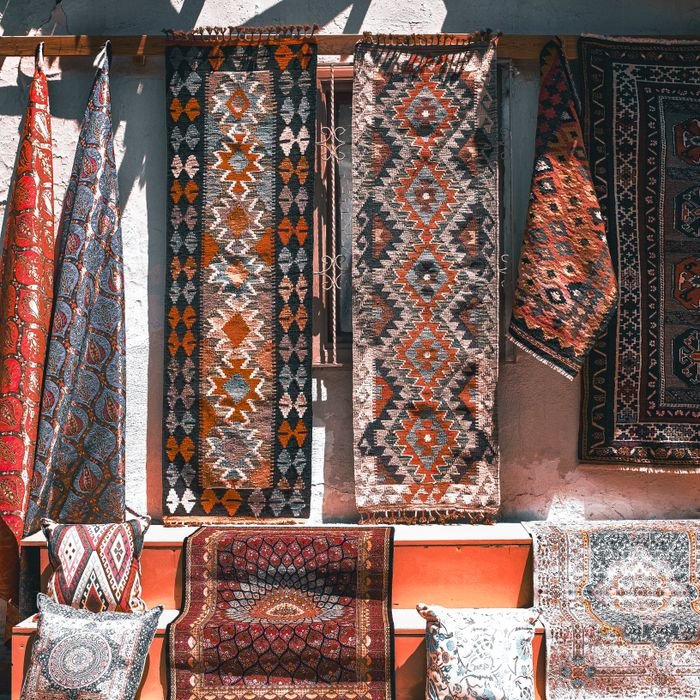 Variety of traditional rugs and textiles with intricate designs displayed in sunlight.